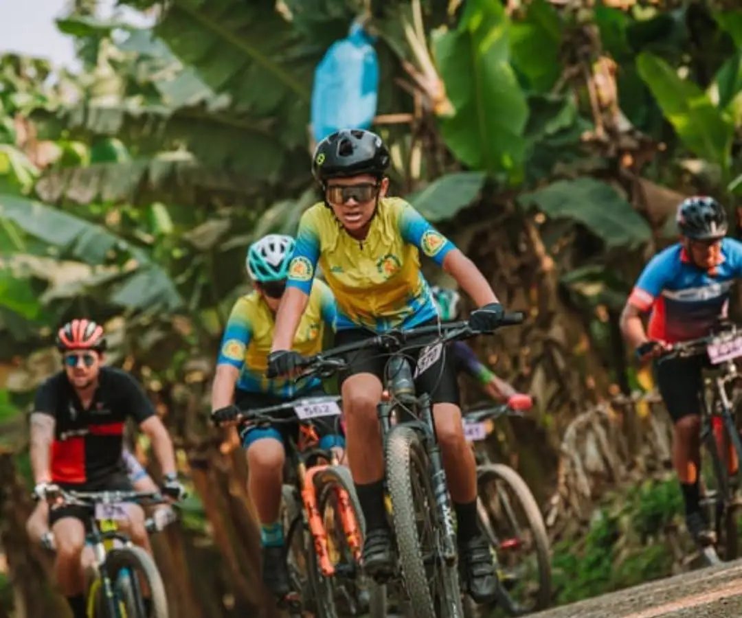 Ciclista da equipe Ciclo Ribeira, de camisa amarela e azul, em prova de MTB no meio do bananal